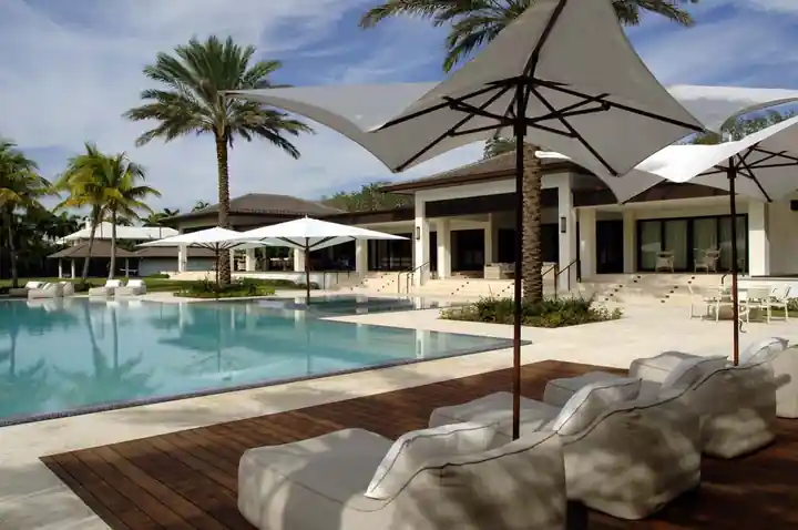Pool and wood deck with sculptural sail shades and loungers at a Gables Estates residence