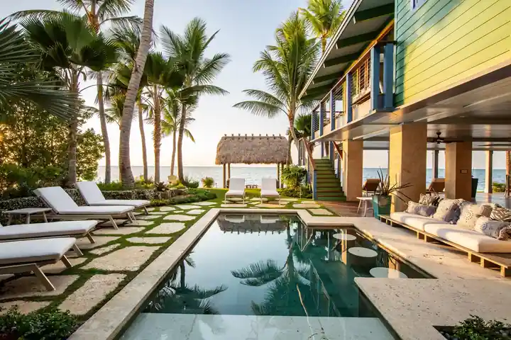 Long pool with grass-jointed pavers, loungers and a tiki hut on the water in Islamorada
