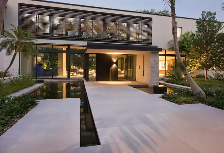 Stepping slabs over a narrow koi pond to a lit modern house at Journeys End