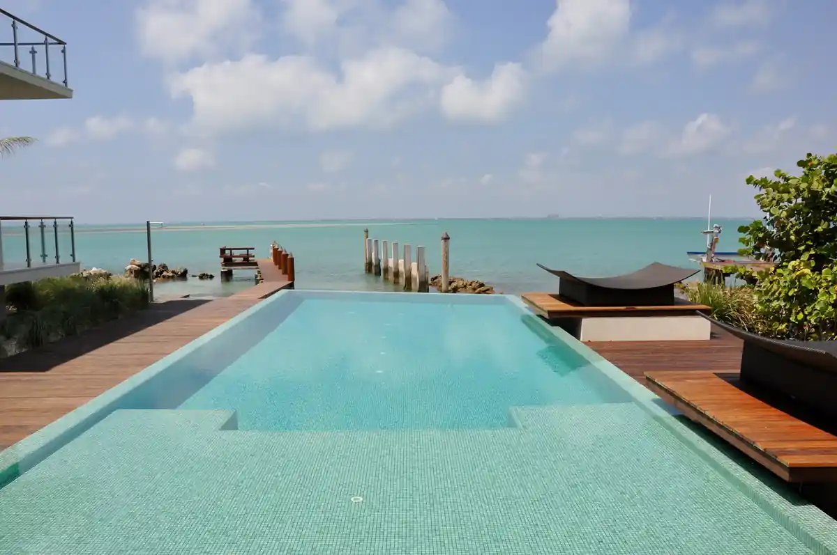 Infinity-edge lap pool in glass tile with a teak deck facing Biscayne Bay