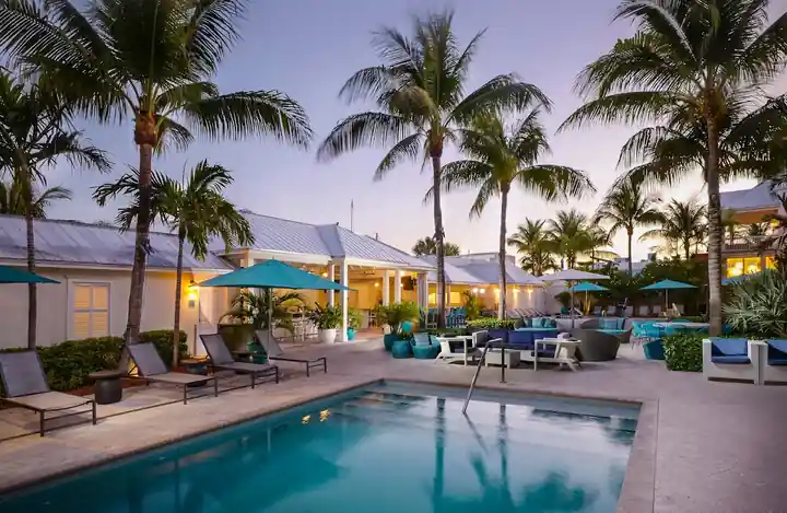 Hotel pool at dusk with lit palms, teal umbrellas and lounge seating at Markers Hotel