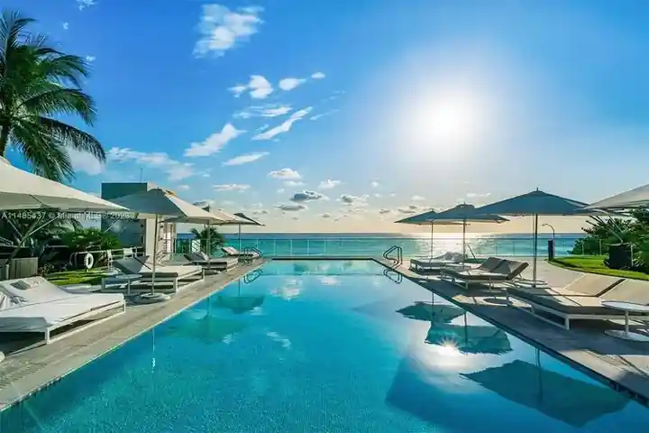 Oceanfront infinity pool with umbrellas and a sun-flared sky at Regalia