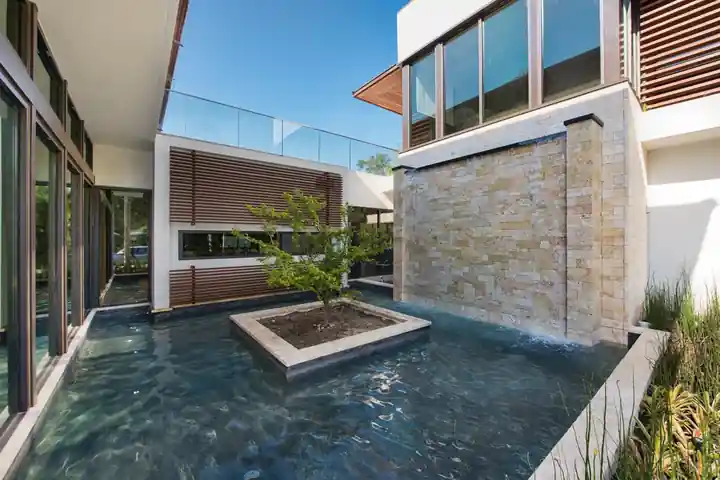 Stone water wall spilling into a reflecting pool beside a modern house in South Miami