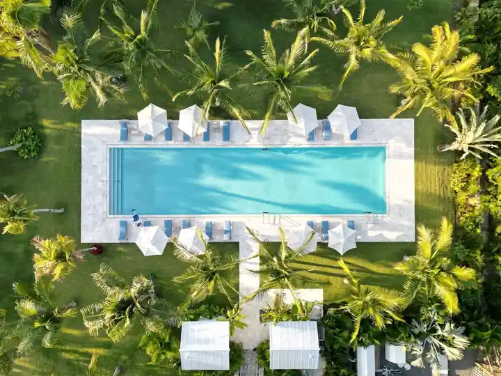 Aerial of a rectangular pool in a white deck ringed by umbrellas and palms at The Moorings